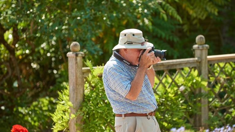A visitor takes photographs in the garden at Compton Castle, Devon on a summer's day